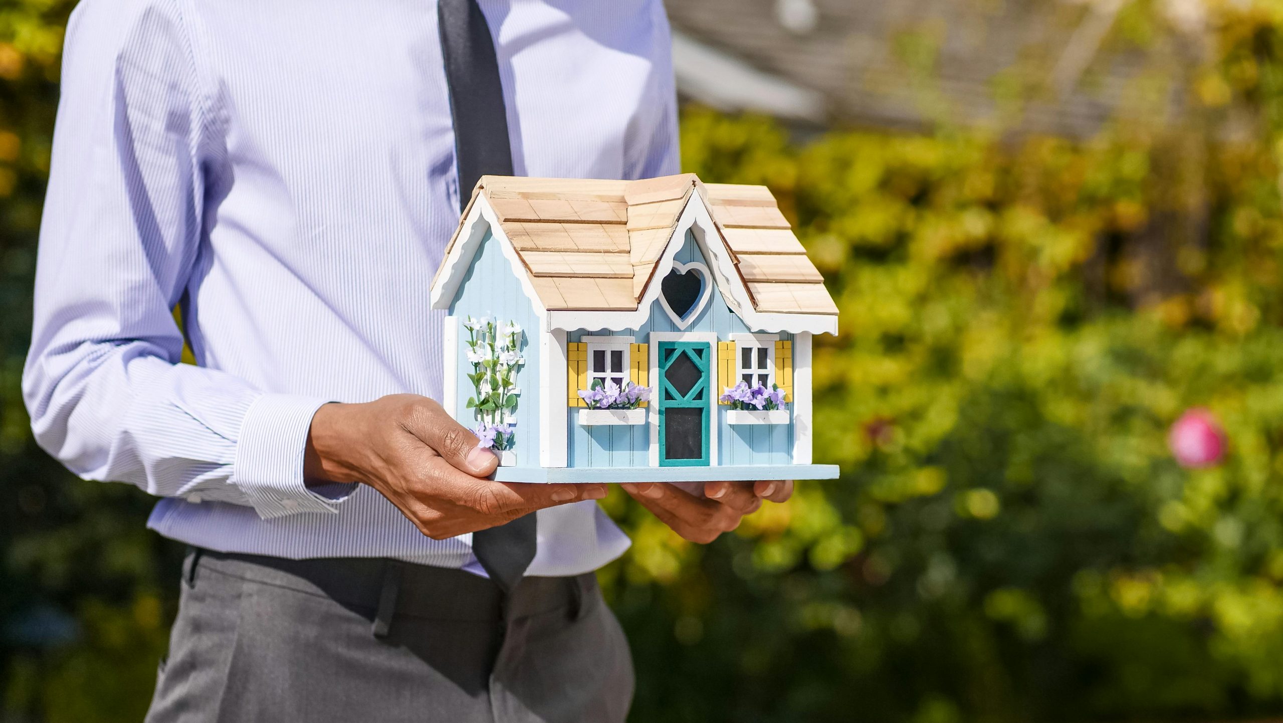 man in a suit holding a model house